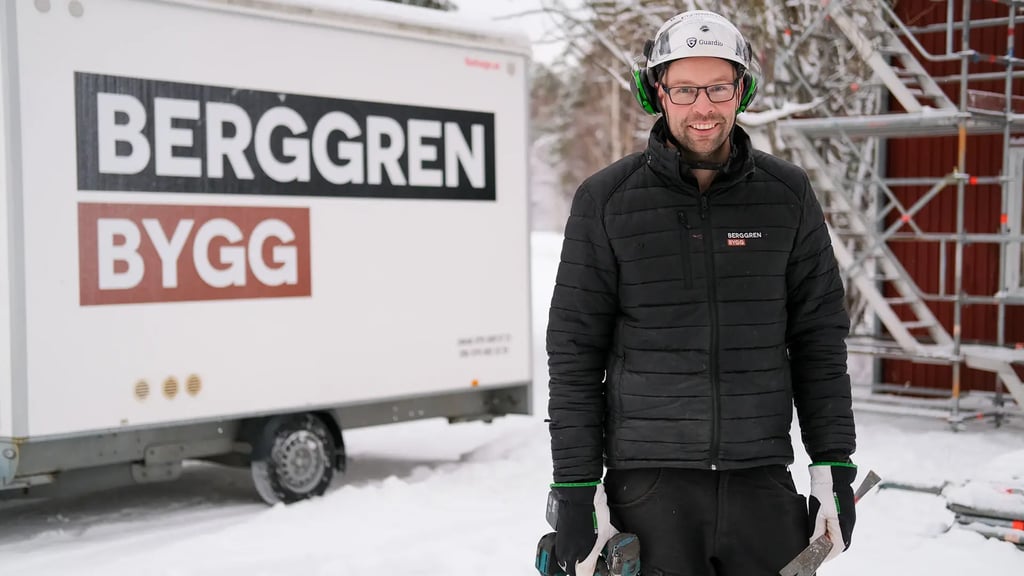 Jakob Berggren från Berggren Bygg står utomhus med en skruvdragare framför ett släp stripat med företagets logotyp.