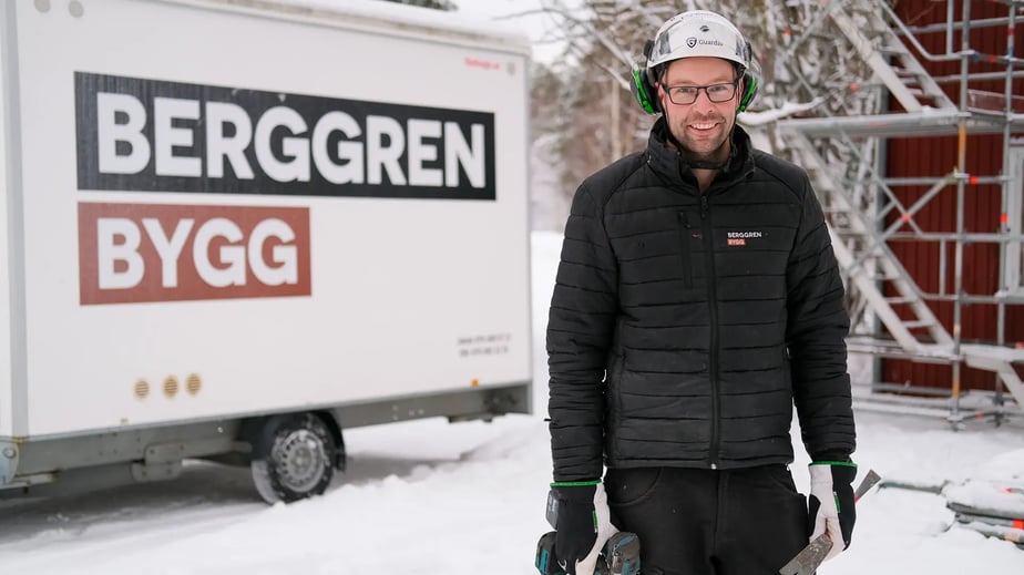Jakob Berggren från Berggren Bygg står utomhus med en skruvdragare framför ett släp stripat med företagets logotyp.