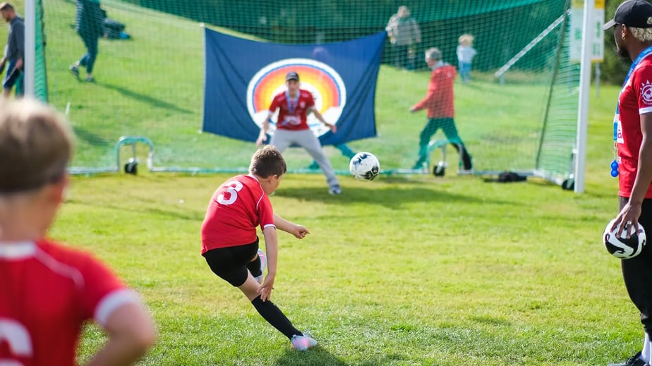 Ögonblicksbild sedd bakifrån på en pojke i röd t-shirt som precis ska lägga en straffspark under Blikk-cupen.